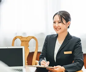 バインダーをもってメモを取りながら笑顔で接客中のスーツの女性